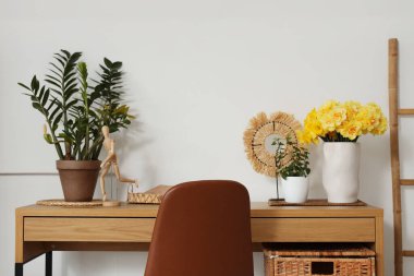 Sarı narsisli çiçekler, ev bitkileri ve ahşap masanın üzerindeki dekorla rahat bir çalışma alanı.