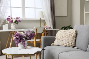 İçinde leylak çiçekleri ve dergi olan vazo oturma odasında.