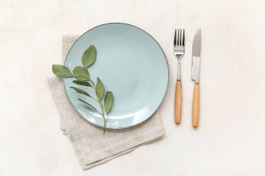 Tabak, peçete, çatal bıçak ve arka planda ağaç dallarıyla güzel bir masa.