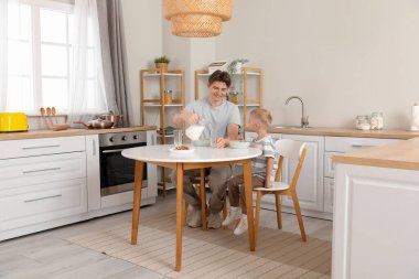 Mutlu baba ve küçük oğlu kahvaltıda mısır gevreği ve süt yiyorlar.