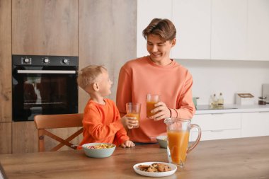 Küçük oğluyla mutlu bir baba mısır gevreği yiyor ve kahvaltıda meyve suyu içiyor.