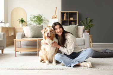 Avustralya çoban köpeği olan genç bir kadın evde yerde oturuyor.