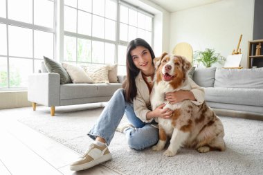 Genç bir kadın evde Avustralya çoban köpeğine sarılıyor.