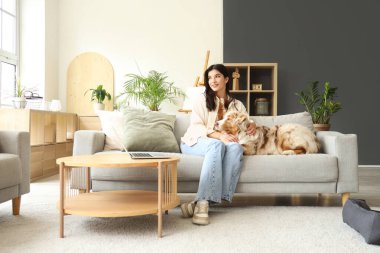 Avustralya çoban köpeği olan genç bir kadın evdeki kanepede oturuyor.