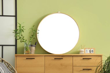 Yeşil duvarın yanındaki ahşap sandıktaki ev ve ayna.