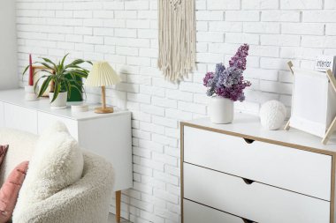 Beyaz tuğla duvarın yanındaki çekmecelerde bir buket leylak dallı oturma odasının içinde.