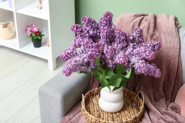 Oturma odasının içinde rahat bir kanepede bir demet leylak dalları var.