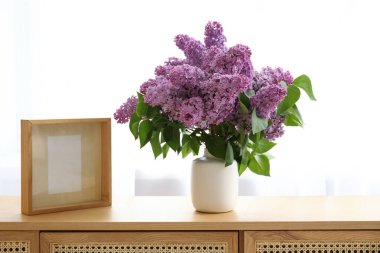 Odadaki çekmecelerin üzerinde leylak dalları olan vazo.