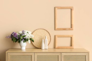 Odadaki bej duvarın yanındaki çekmecelerde leylaklar olan vazo.