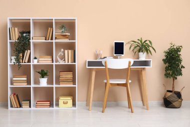 Çalışma odası ve bej duvarın yanında kitaplığı olan modern oturma odasının içinde.