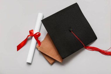 Kırmızı kurdeleli diploma, kitaplar ve beyaz arka planda mezuniyet şapkası.