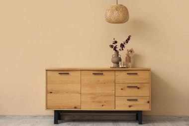 Yapay okaliptüs dallı vazo ve odasındaki bej duvarın yanında ahşap el.