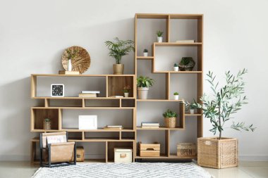 Odasında ışık duvarı yakınında yapay bitkiler olan ahşap bir kitaplık.