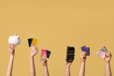 Kredi kartı, cüzdan, domuz kumbarası ve sarı arka planda ödeme terminali olan kadın eller.