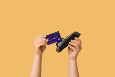 Kredi kartı olan bir kadın sarı arka planda ödeme terminali üzerinden ödeme yapıyor.