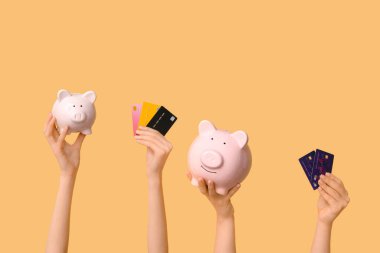 Female hands with credit cards and piggy banks on yellow background