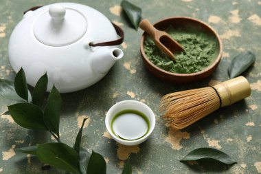 Yeşil zemin üzerinde chasen olan bir kase kibrit çayı ve pudra.