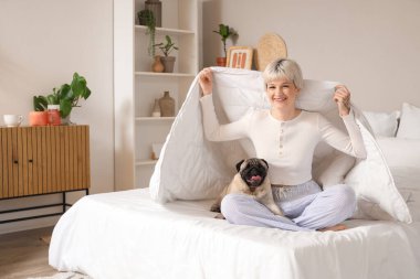 Yatak odasında battaniyeli ve köpekli genç bir kadın oturuyor.