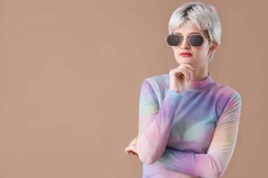 Kahverengi arka planda güneş gözlüklü düşünceli genç bir kadının portresi.