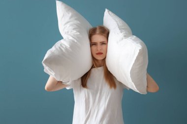 Mavi arka planda uykusuzluk çeken yastıklı genç bir kadın.