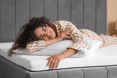 Yatak odasındaki yumuşak yatakta yastıklı genç Afro-Amerikalı kadın.