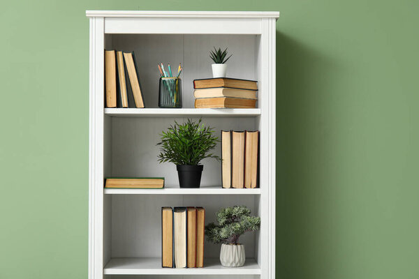 Bookcase with books and houseplants near green wall in room, closeup