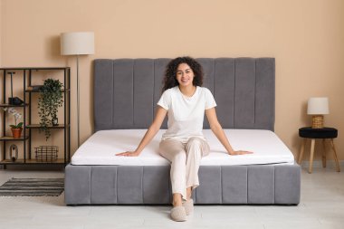 Genç Afro-Amerikalı kadın yatak odasında yumuşak bir yatakta oturuyor.