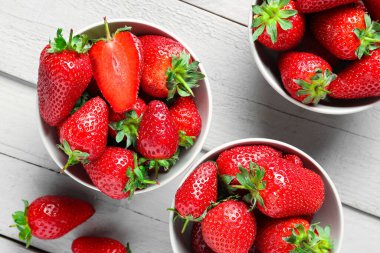 Gri ahşap arka planda taze çilekli kaseler.