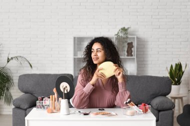 Güzel, mutlu, kozmetik çantalı Afro-Amerikan kadın evde makyaj yapıyor.