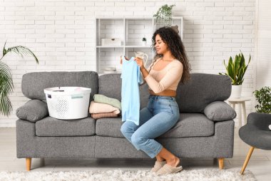 Çamaşır sepetiyle evde temiz giysileri katlayan güzel, mutlu, Afro-Amerikalı bir kadın.