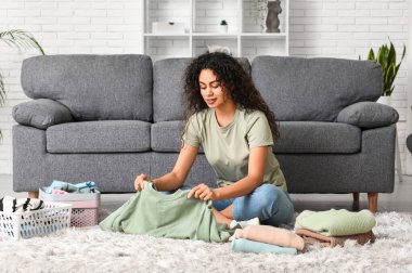 Güzel, genç, mutlu, Afro-Amerikan kadın. Temiz giysileri evde katlıyor.