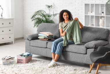 Güzel, genç, mutlu, Afro-Amerikan kadın. Temiz giysileri evde katlıyor.