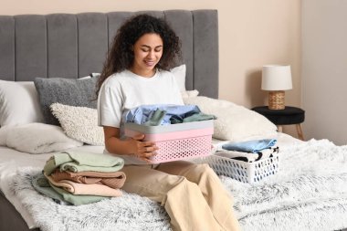 Güzel, genç, mutlu, Afro-Amerikan bir kadın yatak odasında temiz giysiler katlıyor.