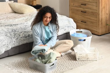 Güzel, genç, mutlu, Afro-Amerikan bir kadın. Elinde sepetler, temiz giysileri katlıyor.