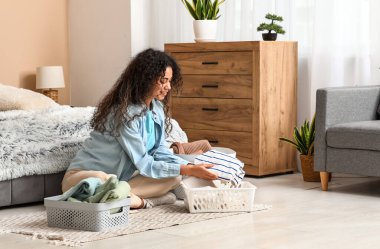 Güzel, genç, mutlu, Afro-Amerikan bir kadın. Elinde sepetler, temiz giysileri katlıyor.