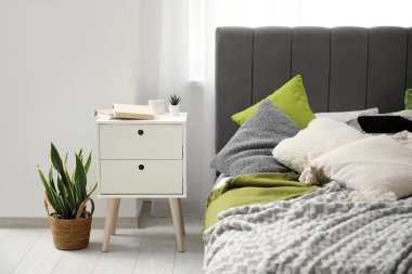 Yatak odasındaki rahat yatağın yanında kitap olan komodinin yanında.