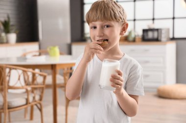 Mutfakta bir bardak sütle kurabiye yiyen şirin bir çocuk.