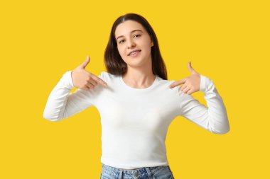 Güzel genç bayan sarı arka plandaki beyaz koluna işaret ediyor.