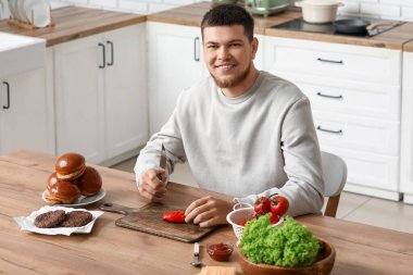 Genç adam mutfakta domates doğruyor.