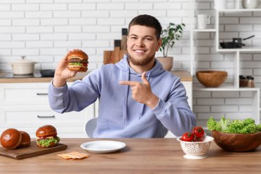 Genç adam mutfaktaki lezzetli burgeri işaret ediyor.