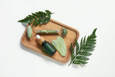Serumlu Jade silindiri, gua sha ve yeşil yapraklar beyaz arkaplanda