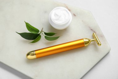 Yüz masajı silindirli taş tahta, kozmetik krem ve gri arka planda yapraklar.