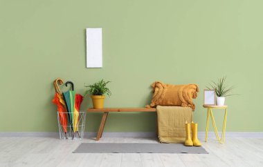 Ahşap bank, sehpa, yastık ve şemsiyeler şık bir odada yeşil duvarın yanında.