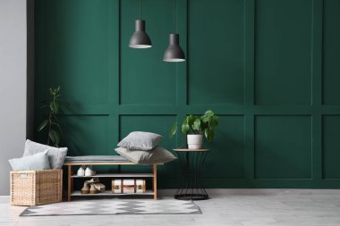 Güzel odada yeşil duvarın yanında rahat bir bank, ayakkabı, yastık ve lamba.