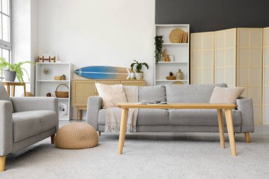 Oturma odasının içinde kanepeler, masa ve sörf tahtası var.