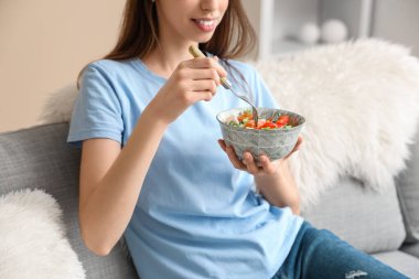 Şık bir oturma odasında salata yiyen genç bir kadın.