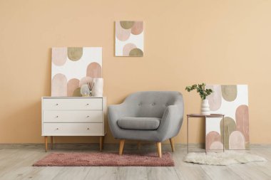 Gri koltuk, beyaz çekmece sandığı ve oturma odasındaki bej duvarda güzel resimler.