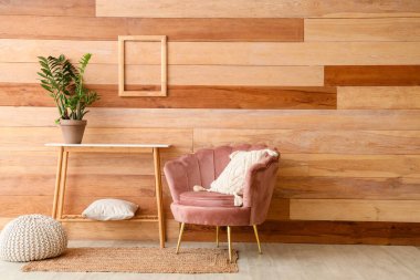 Ahşap duvarın yanında pembe koltuk ve konsol masası.