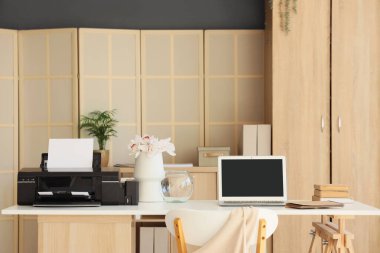 Ofisinde çiçekler ve dizüstü bilgisayarı olan modern bir yazıcı