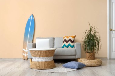 Sörf tahtası, rahat kanepe ve oturma odasında dizüstü bilgisayarı olan bir sehpa.